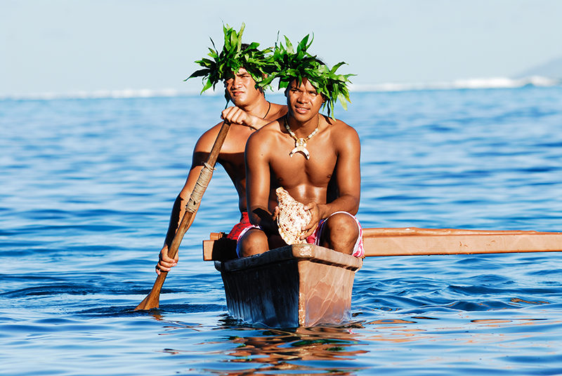 Jeunes polynsiens en costume traditionnel sur une pirogue, dans le lagon de Tahiti.