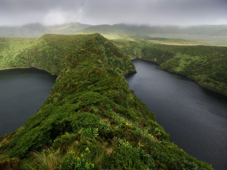 Lush green hills surround dark blue lakes under cloudy sky