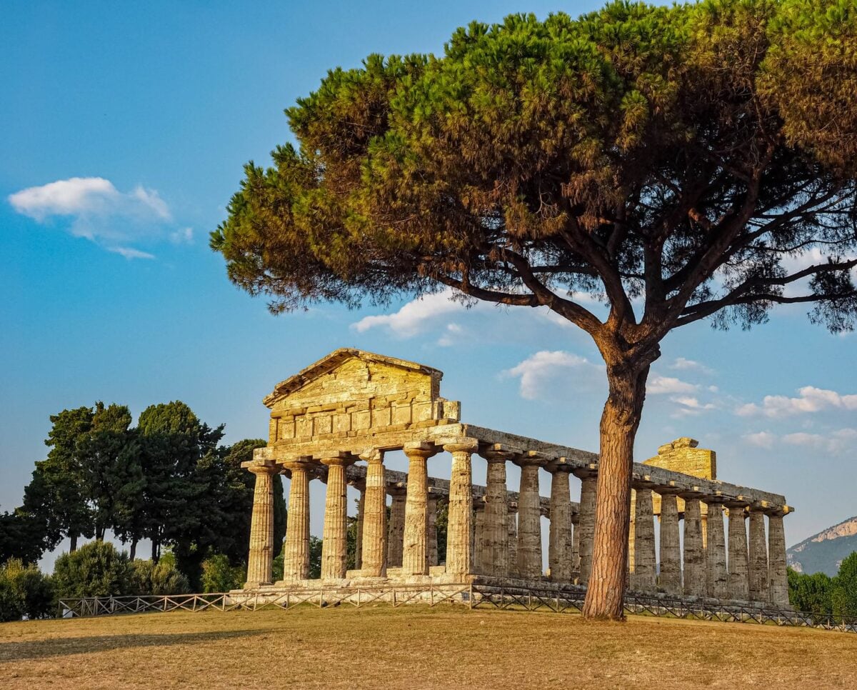 Explore the majestic ruins of an ancient Greek temple with lush greenery and a golden sunset.