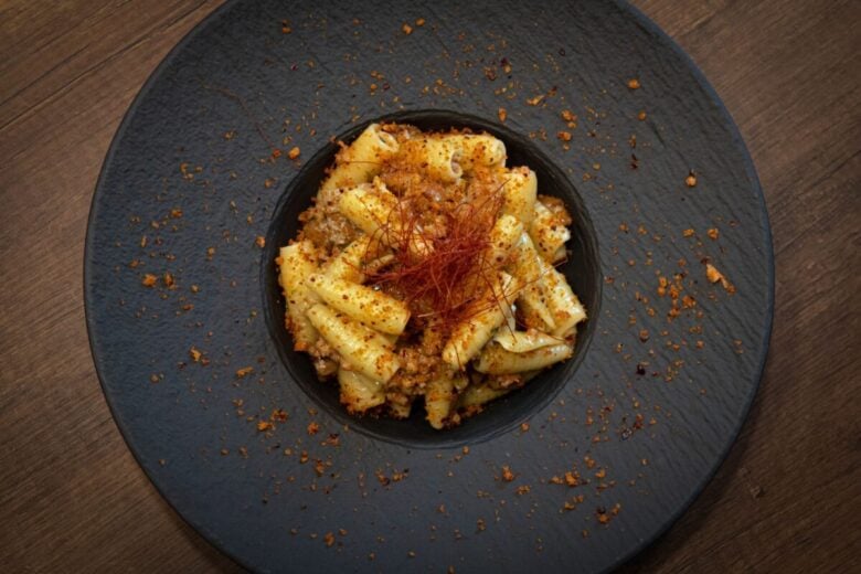Delicious rigatoni pasta with spices served on a rustic black plate.