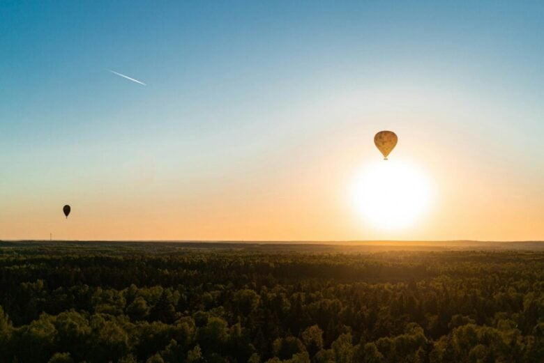 a hot air balloon flying over a forest at sunset