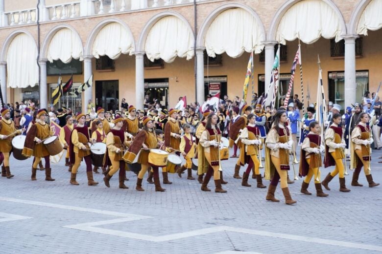 A lively medieval parade with musicians and flags in Faenza's historic streets.