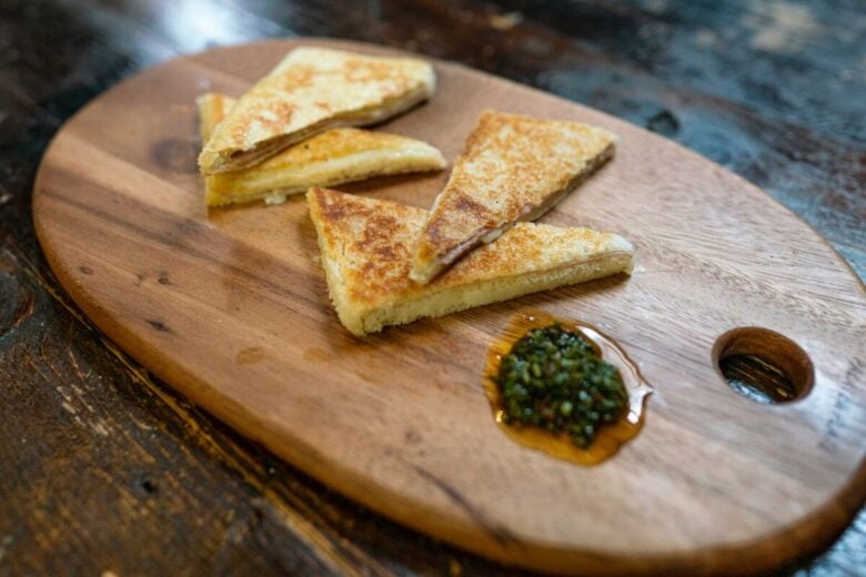 Golden grilled cheese sandwiches on a wooden board served with a side of green chutney.