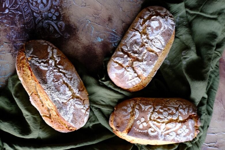 Top-down view of three artisan bread loaves on a rustic surface, showcasing intricate flour patterns and fresh appearance.