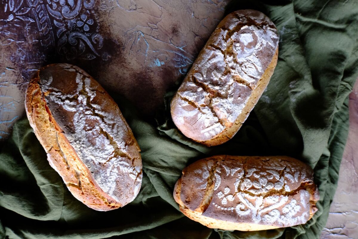 Top-down view of three artisan bread loaves on a rustic surface, showcasing intricate flour patterns and fresh appearance.