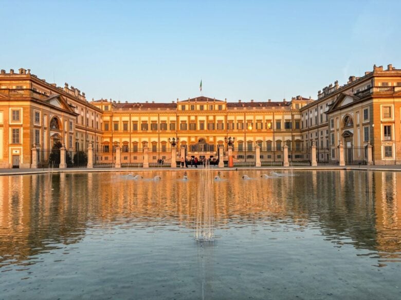 The elegant Royal Villa of Monza reflecting in a tranquil fountain during a golden sunset.
