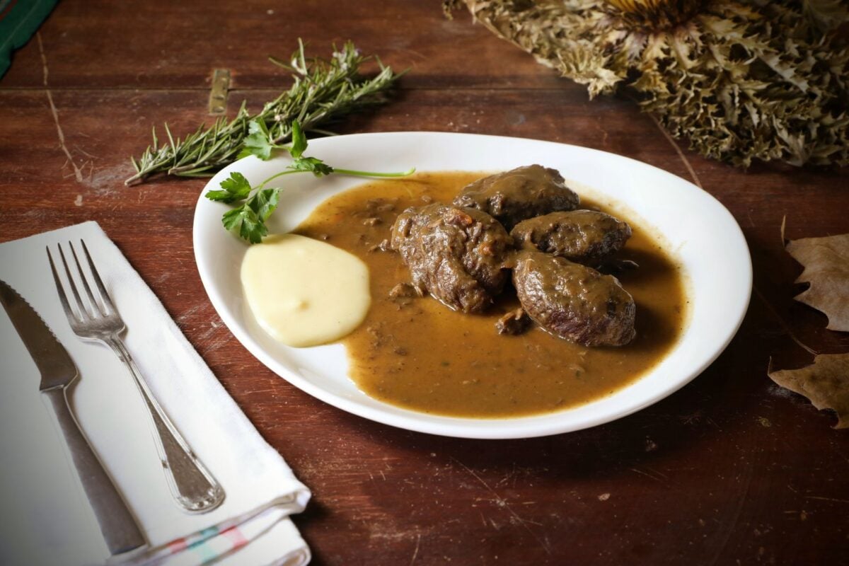 Delicious herb-crusted beef served with gravy and creamy mashed potatoes on a rustic table setting.