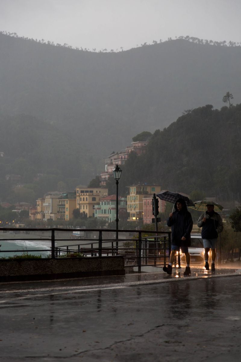 Two people walk with umbrellas in a scenic Italian coastal town during a rainy day.