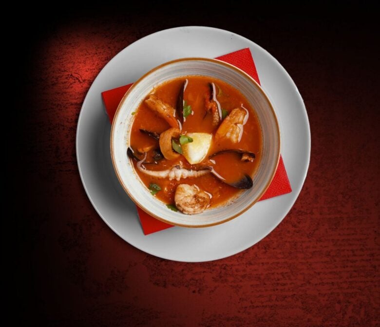 A rich seafood stew served in a bowl with a red backdrop. Perfect for gourmet food representation.