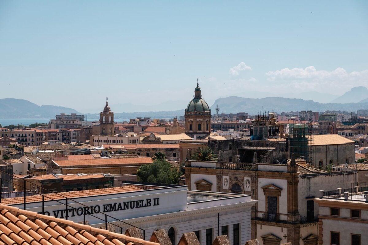 Captivating view of Palermo's historic architecture against a mountainous backdrop under a clear sky.