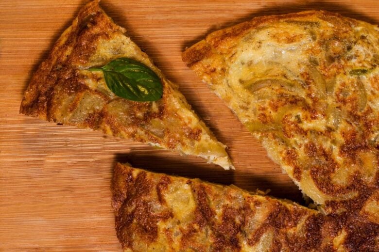 Close-up of traditional Spanish tortilla slices on a wooden board, garnished with basil.