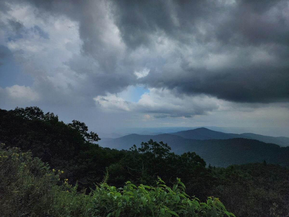 A cloudy sky over a mountain range with trees in the foreground