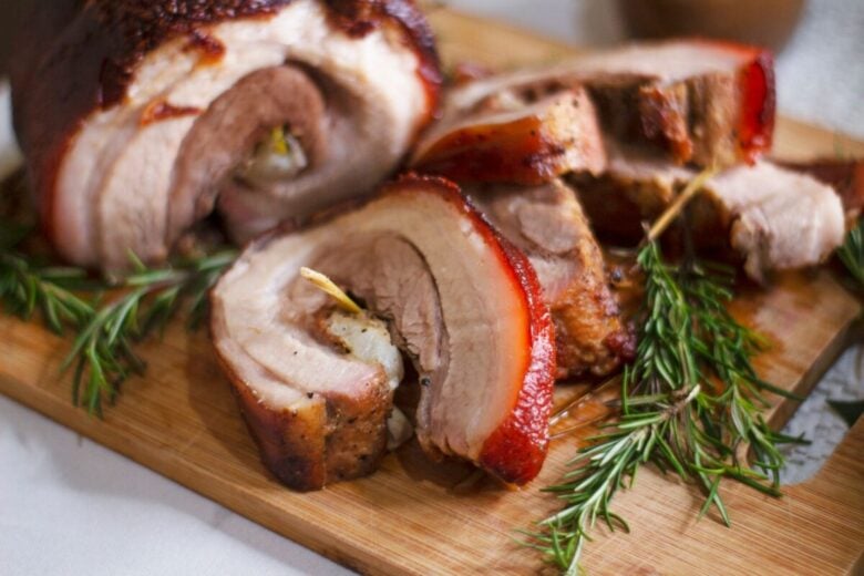 Delicious roasted porchetta slices on a wooden board with rosemary garnish, showcasing Italian cuisine.