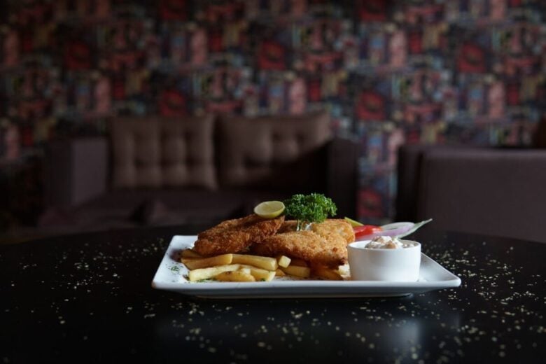 Crispy fish and chips served with garnish and dip in a cozy indoor setting.