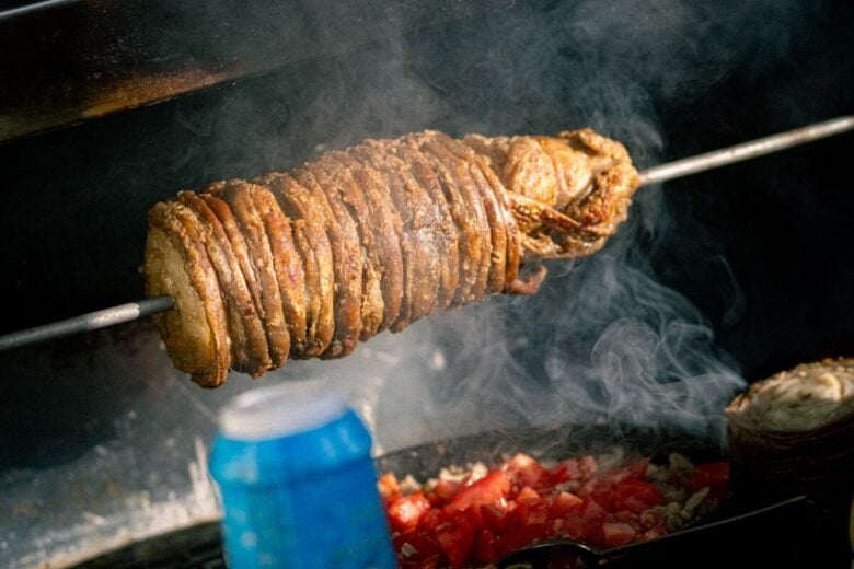 Juicy kokoretsi skewer rotating on a grill with tomatoes and smoke rising.