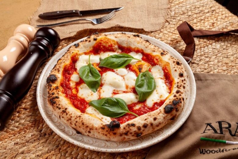 Delicious wood-fired Margherita pizza topped with fresh basil leaves and mozzarella cheese.
