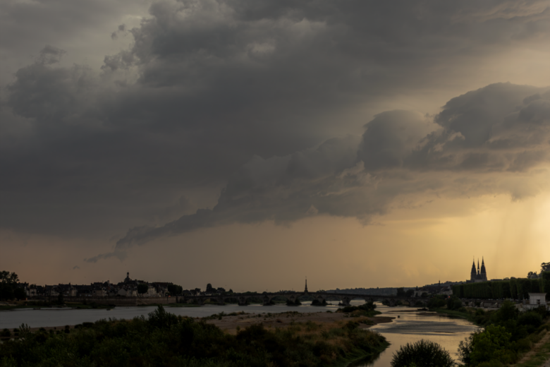 A moody landscape featuring a river under dramatic storm clouds at sunset.