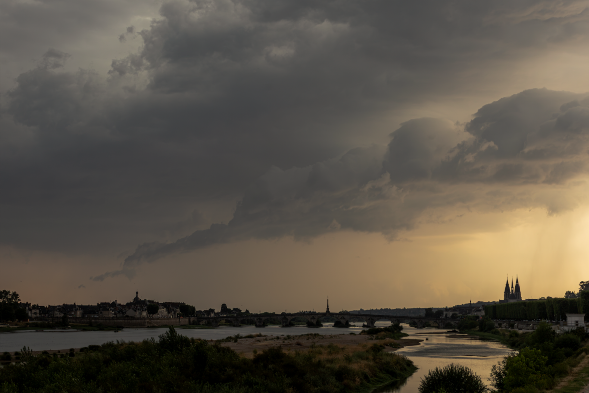 A moody landscape featuring a river under dramatic storm clouds at sunset.