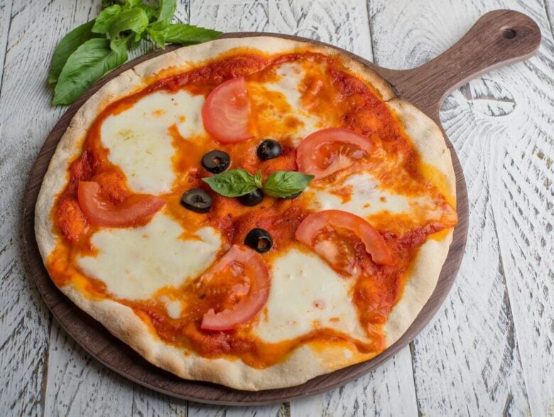 Appetizing Margherita pizza with tomatoes, olives, and fresh basil on a wooden board.