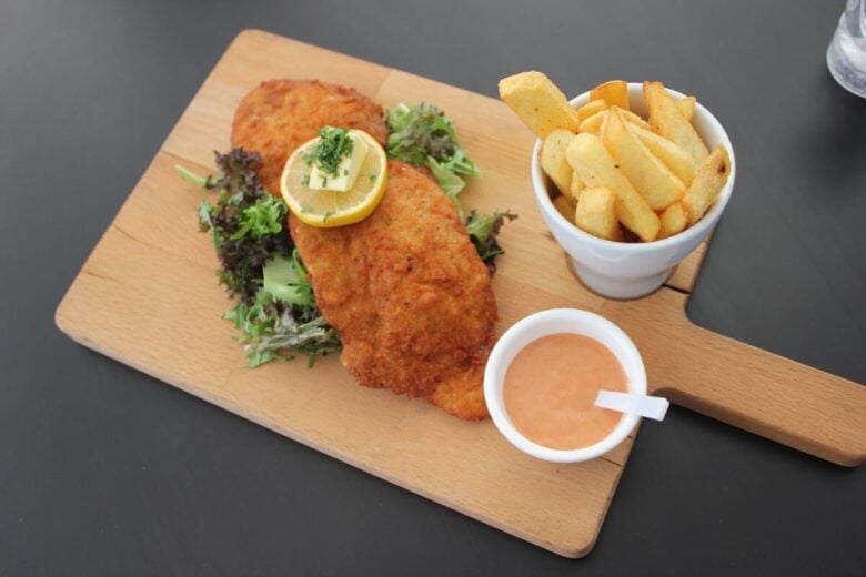 Crispy fried chicken with lemon, fresh salad, fries, and sauce on a wooden board.