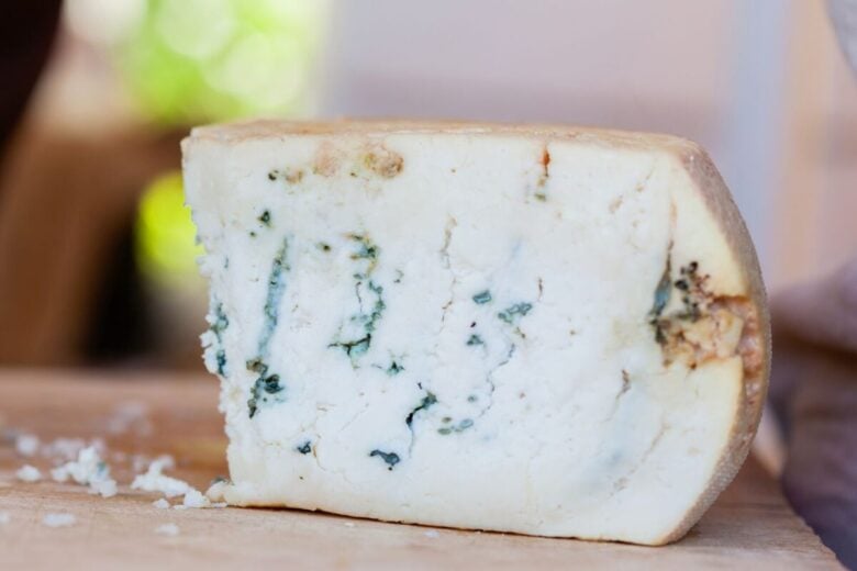A detailed close-up shot showcasing a wedge of artisan blue cheese with a natural rind on a wooden board.