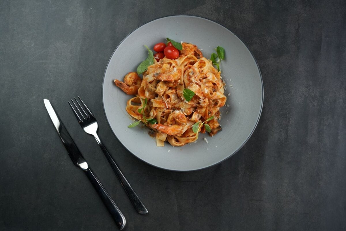 Top-down view of shrimp pasta with basil and cherry tomatoes on a plate.