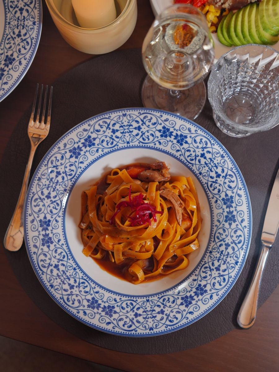 Close-up of tagliatelle pasta dish with tomato sauce and vegetables, set on an elegant table.