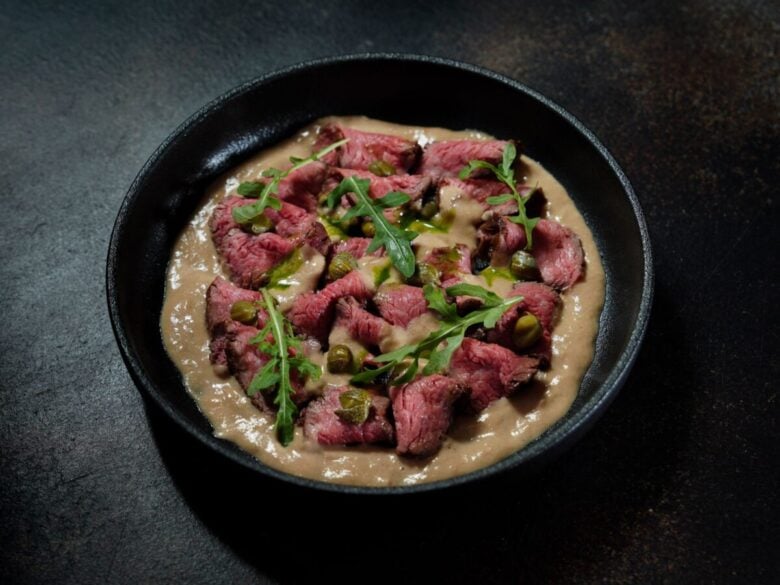 Delicious gourmet beef dish with arugula and rich sauce presented in a dark bowl for elegant dining.