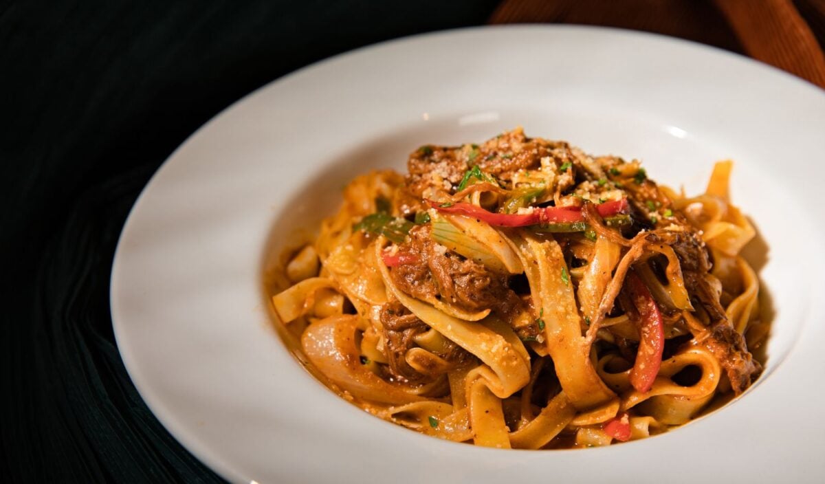 Close-up of a flavorful pasta dish in a white bowl with rich sauce and garnishes.