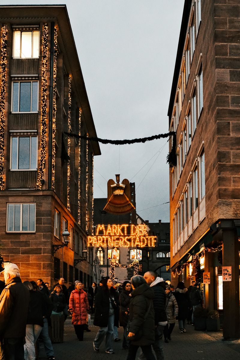 Vibrant Christmas market street with illuminated decorations and shoppers in a winter setting.