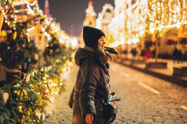 Woman joyfully embraces the festive Christmas lights on a wintry night.