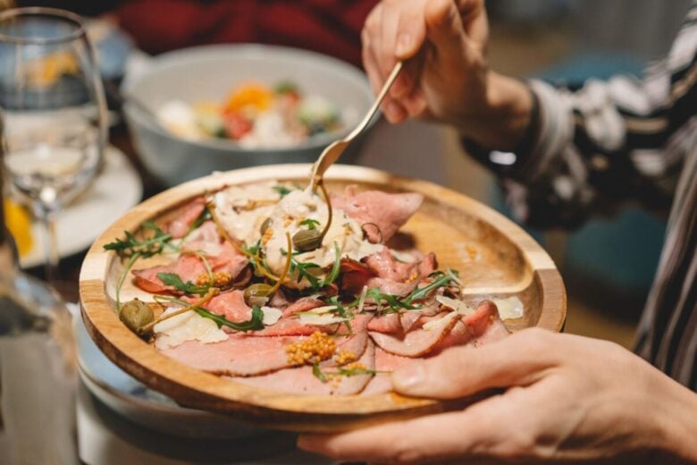 Close-up of a delicious sliced meat platter topped with arugula and capers, served on a wooden tray.